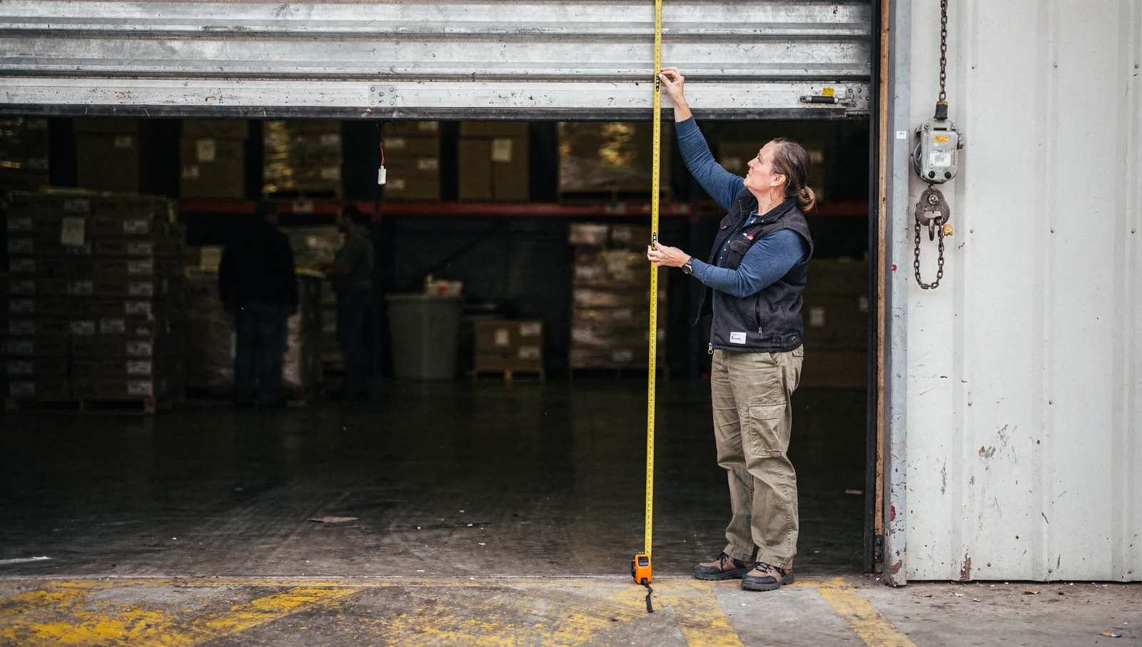 A woman uses a yellow tape measure to check the clearance height of an industrial loading dock door.